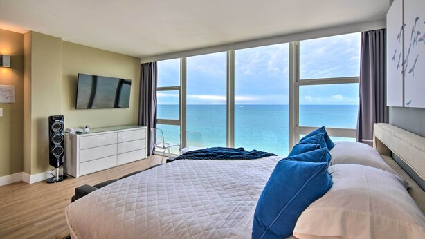 A hotel room with a large bed, a TV, a desk, and a view of the ocean. - Oceanfront Luxury 2/2 Condo w/ Amazing Views! (Fort Lauderdale)