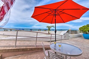 A beachside patio with a red umbrella, a table with a drink, and a view of the ocean. - Oceanfront Luxury Renovated Resort Getaway! (Fort Lauderdale)
