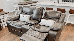Un sofá de cuero reclinable con reposapiés y portavasos, ubicado en una sala de estar moderna con piso de madera y mobiliario blanco.