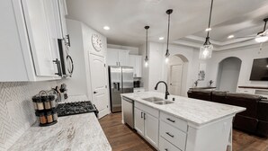 Una cocina moderna con armarios blancos, una isla central con fregadero y un refrigerador de acero inoxidable.