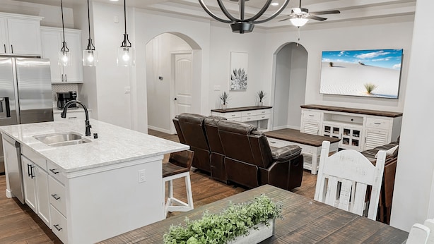 Una cocina moderna con una isla central, armarios blancos y un comedor con mesa y sillas de madera.