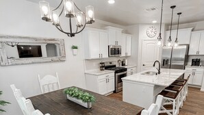 Una cocina moderna con armarios blancos, electrodomésticos de acero inoxidable y una mesa de comedor de madera con sillas blancas.
