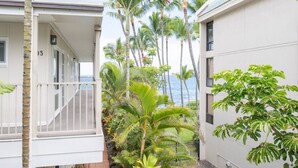 A residential building with a balcony, surrounded by palm trees and a view of the ocean.