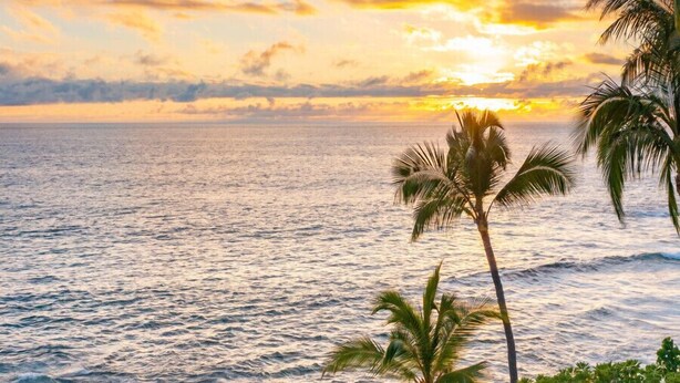 A poolside area with lounge chairs and a view of the ocean at sunset.