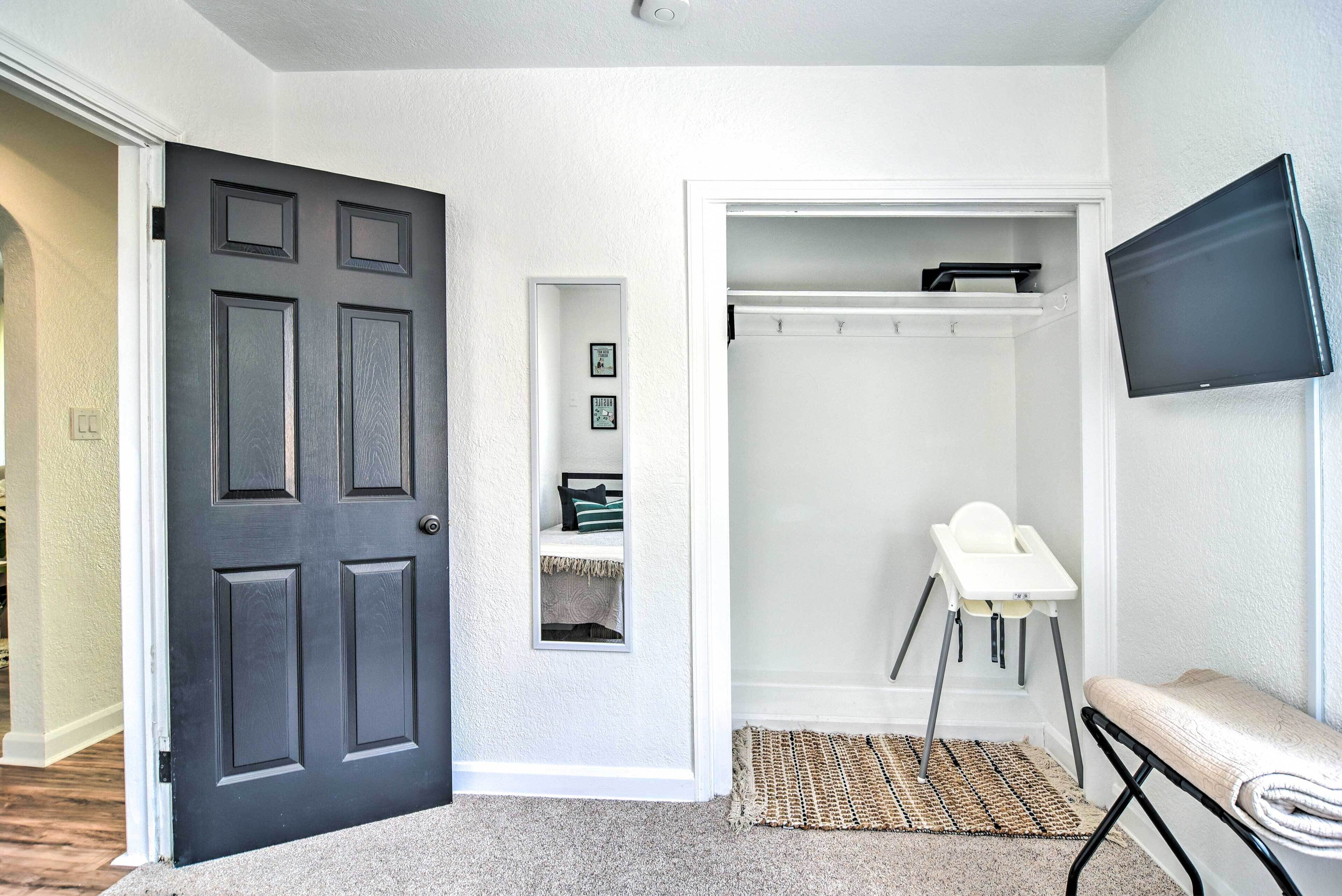 A hallway with a dark door, a white closet with shelves, a baby high chair, and a TV mounted on the wall.