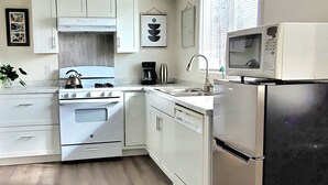 Une cuisine de taille réduite, dotée de meubles blancs, d’une cuisinière à gaz, d’un four à micro-ondes et d’un lave-vaisselle.