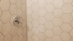 Une douche avec des carreaux hexagonaux et un pommeau de douche à main.