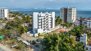 A multi-story hotel with a modern design, located near a coastal area with palm trees and a view of the ocean.