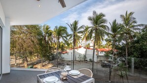 A balcony with a table set for dining, overlooking a palm tree-lined area with buildings in the background.