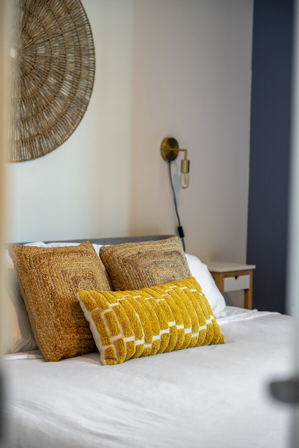 A neatly made bed with two textured pillows, a wall-mounted light fixture, and a small bedside table.
