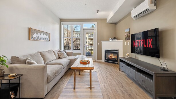 Een woonkamer met een beige bank, een houten salontafel en een flatscreen televisie aan de wand.