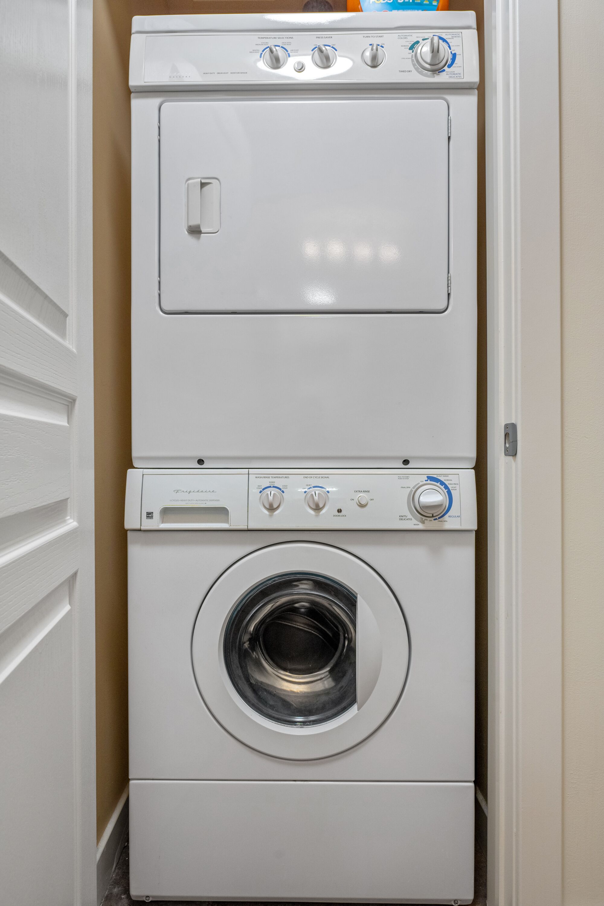 Lavadora de carga frontal con panel de control, una secadora encima y una puerta a la izquierda.