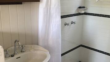 Een badkamer met een witte wastafel, een spiegel, een douche met een zwart-wit schaakbordvloer en een wit gordijn.