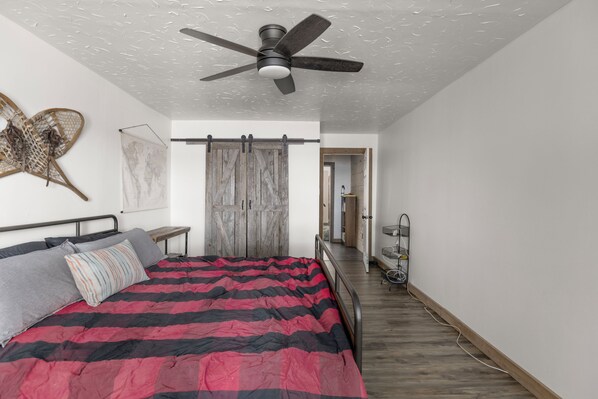 Une chambre à coucher avec un lit, un ventilateur de plafond, une porte en bois et une carte du monde accrochée au mur.