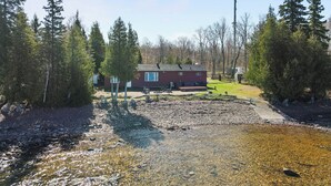 Une cabane dotée d’une terrasse, entourée d’arbres et bordée par un ruisseau aux eaux claires.