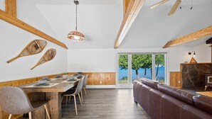 Un espace repas avec une table et des chaises en bois, un canapé en cuir et une vue sur la mer grâce à de grandes portes vitrées.