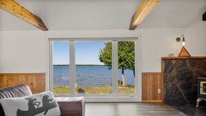 Une pièce dotée d’une grande fenêtre donnant sur un lac, d’un plafond en bois, d’un canapé en cuir marron et d’une table basse en bois.