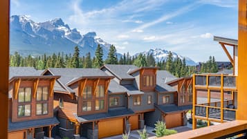 Une rangée de maisons de style chalet en bois, dotées de grandes fenêtres, d’une terrasse et surplombant un paysage montagneux.