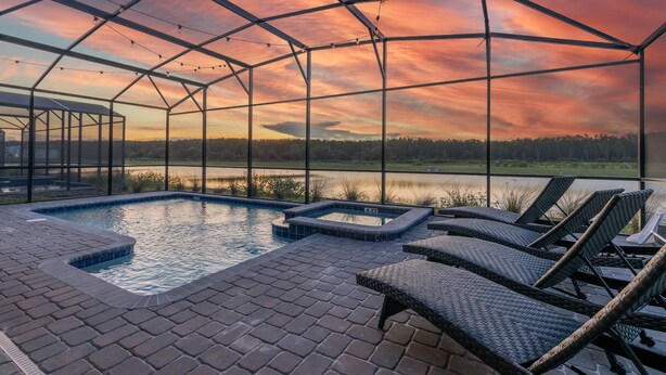 A pool area with lounge chairs and a view of a lake at sunset.