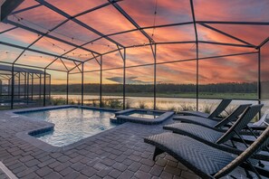 A pool area with lounge chairs and a view of a lake at sunset. - Luxury Lakeview Villa with Game Room + Theater & Free Waterpark Close to Disney  (Kissimmee)