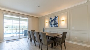 A dining area with a large table and chairs, a view through glass doors, and wall-mounted lighting.