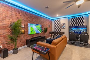 Ein modernes Wohnzimmer mit einer Ziegelwand, einem großen Flachbildfernseher, einer Spielkonsole und einem bequemen orangefarbenen Sofa.