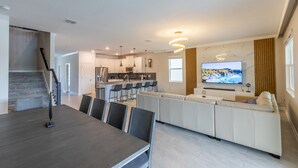 A modern living room with a dining area, a kitchen, and a TV.