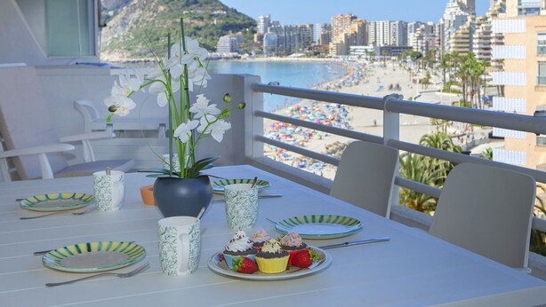 A balcony with a table set for a meal, overlooking a beach and cityscape. - Beautiful apartment for 6 people with pool, A/C, WIFI, TV and terrace (Calpe)