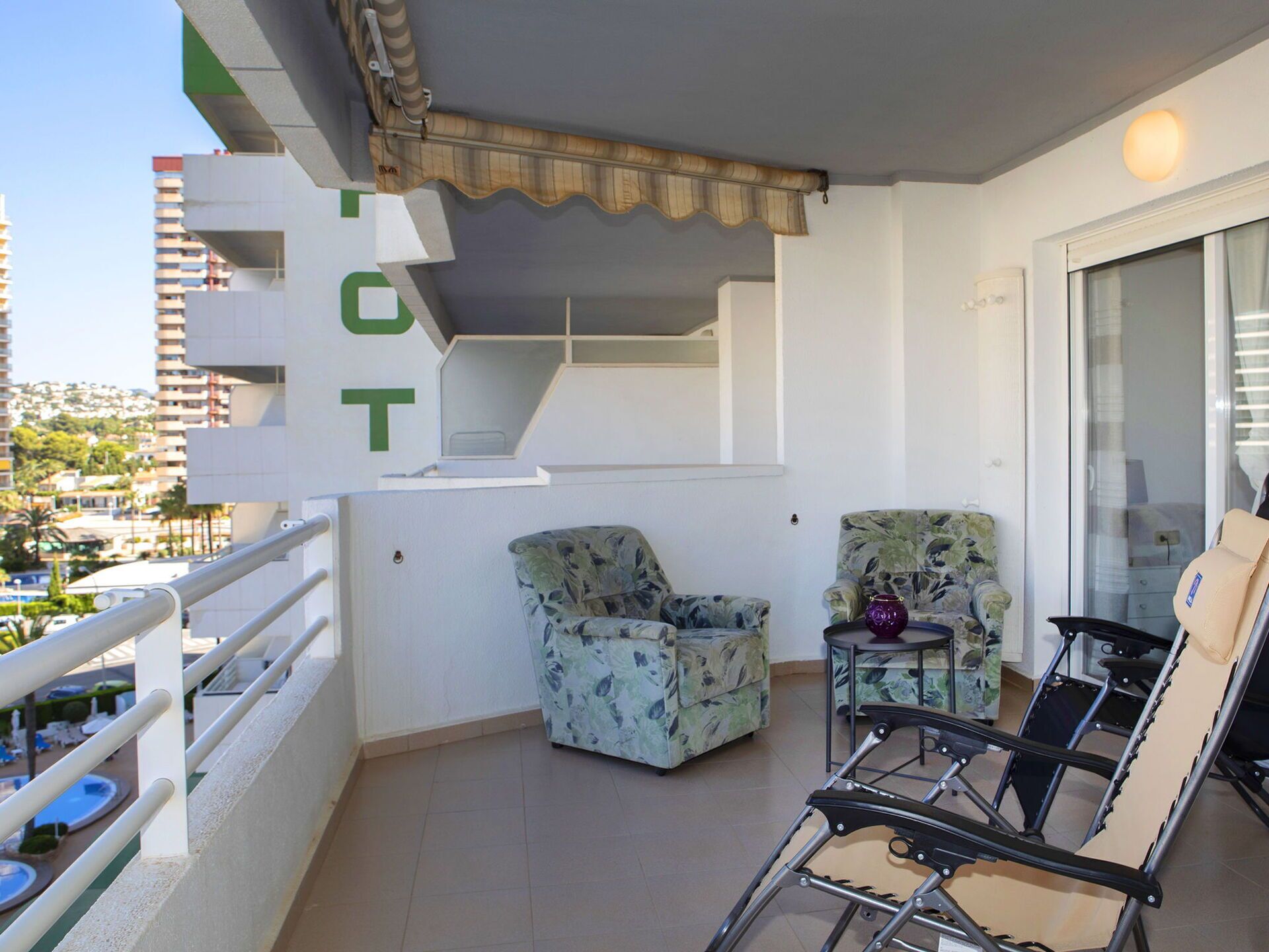 A balcony with two patterned armchairs, a small table, and a folding chair.