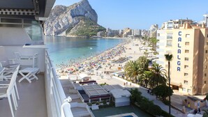 A balcony with white chairs and a pool area, overlooking a beach with umbrellas and a building labeled "CALALGA". - Beautiful apartment for 6 people with pool, A/C, WIFI, TV and terrace (Calpe)