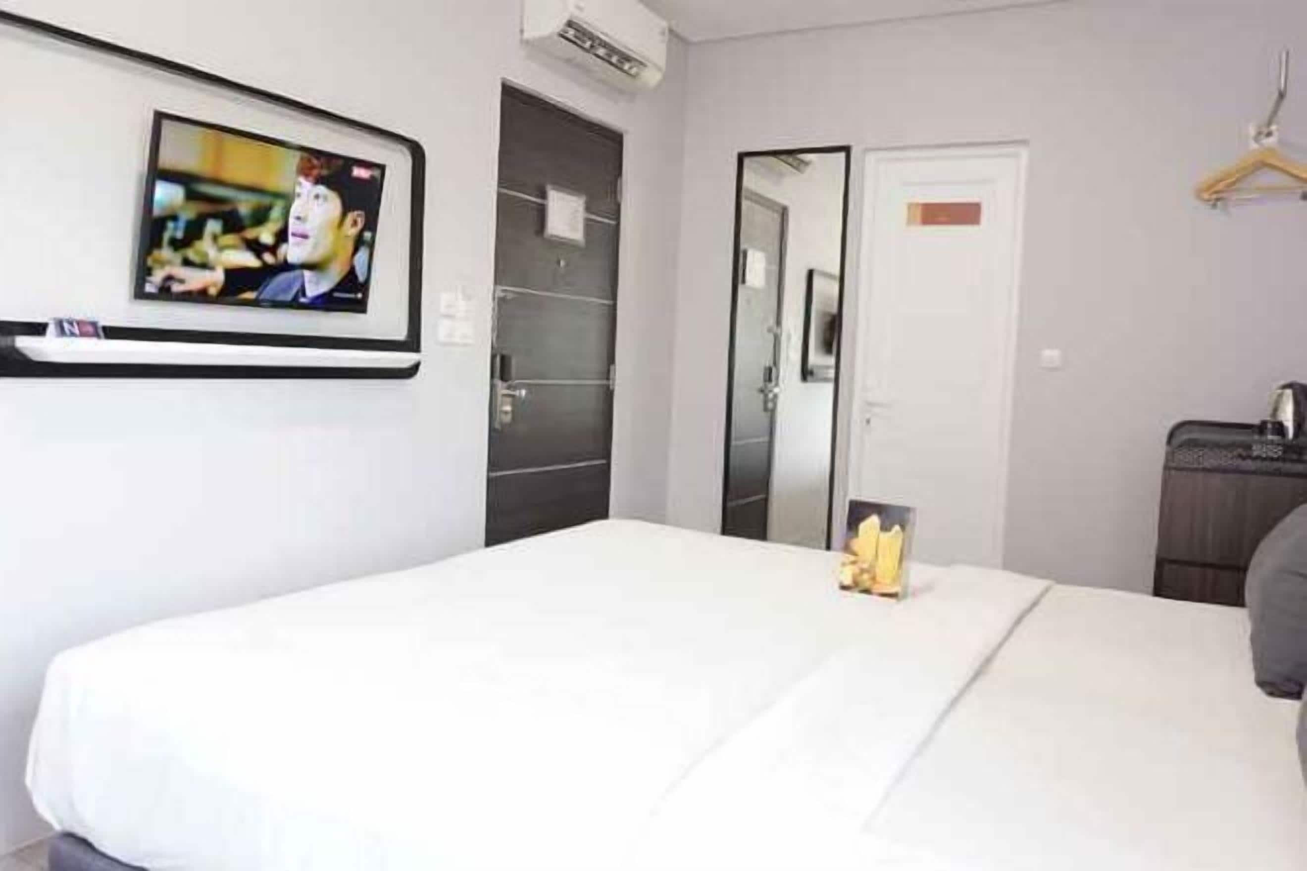 A hotel room with a bed, a TV mounted on the wall, a mirror, and a wardrobe.