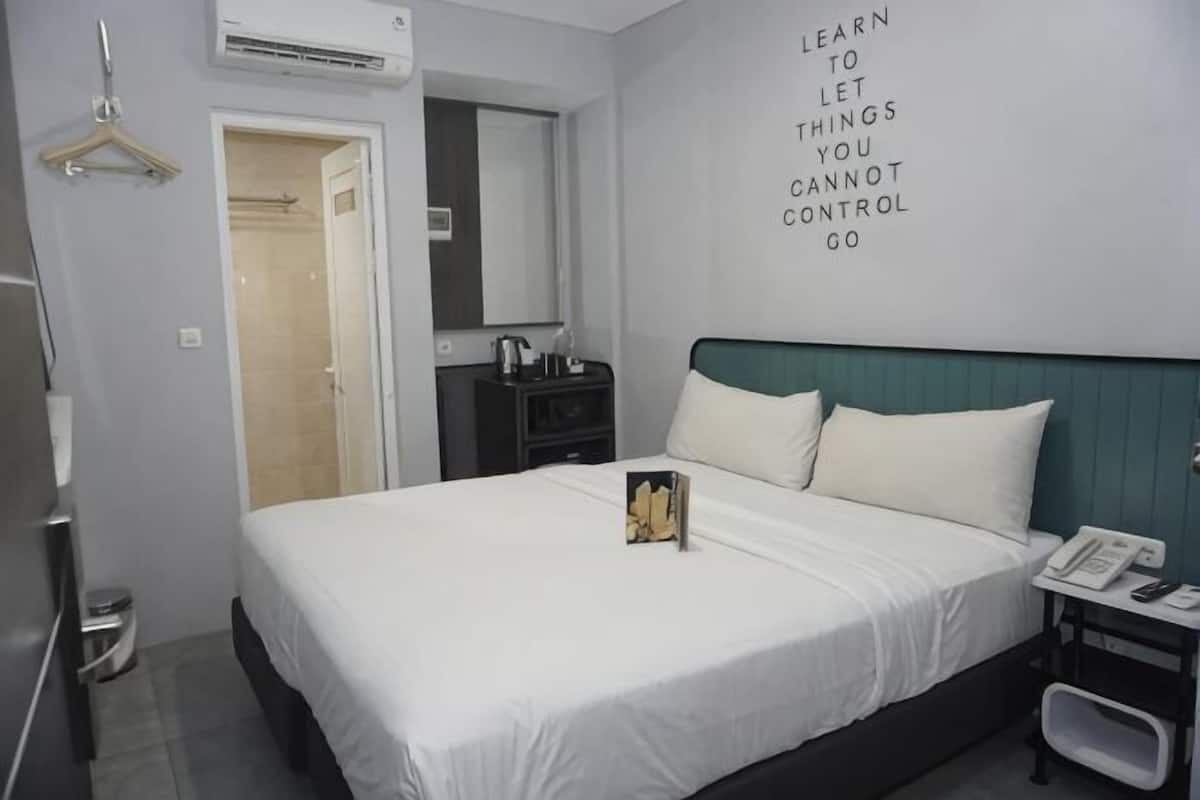 A hotel room with a bed, a bedside table with a phone, a mirror, and a wall with a motivational quote.