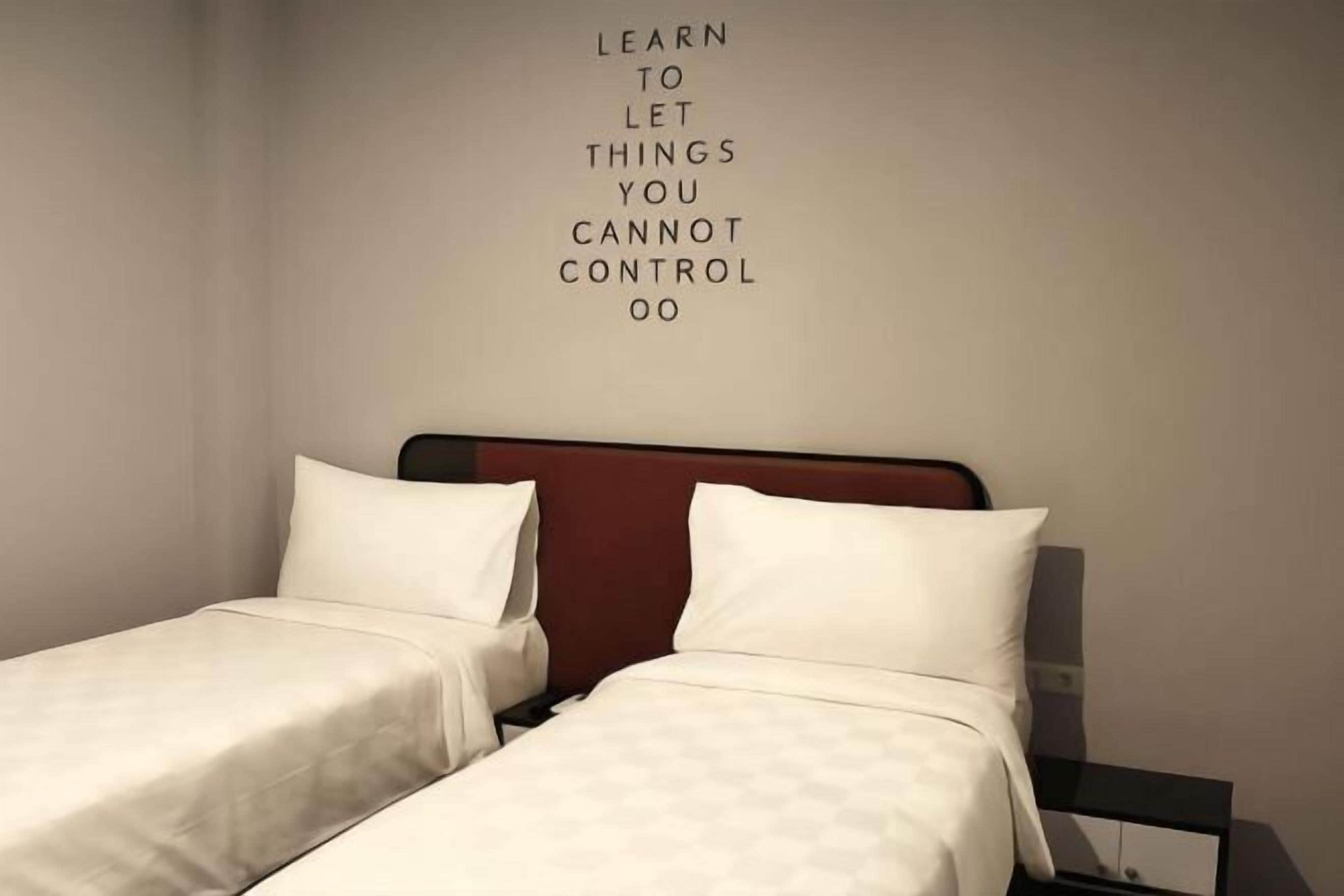 A hotel room with two beds, a red headboard, and a motivational quote on the wall.