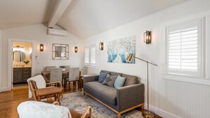 A spacious living room with a gray sofa, wooden chairs, a coffee table, and a large painting on the wall.