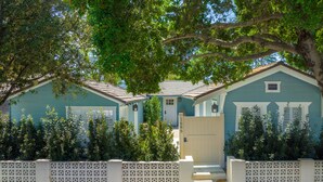 A row of two-story houses with a white fence in front, each with a small front porch and a door visible.