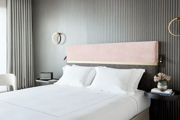Een hotelkamer met een groot bed, een nachtkastje met een lamp, een klein bijzettafeltje met een bloevas en een rond plafondlicht.