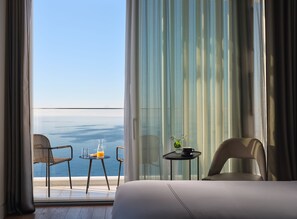 A hotel room with a balcony, a bed, two chairs, a small table with a glass of orange juice and a cup, and a vase with flowers.