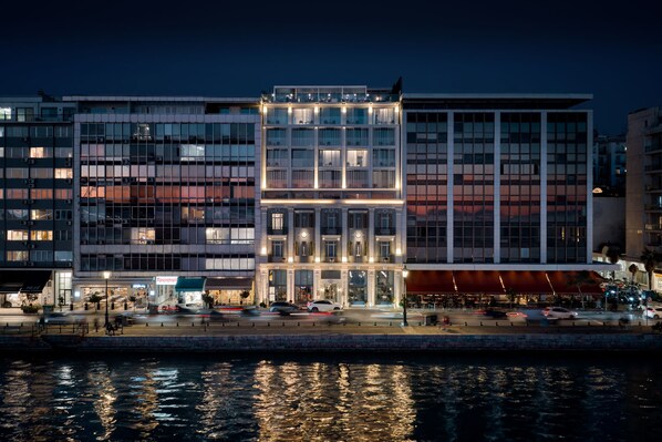 Un hotel moderno con fachada de vidrio, entrada central y vistas al agua.