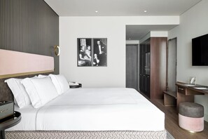 A modern bedroom with a large bed, a bedside table, a desk, and a TV mounted on the wall. - ON Residence (Thessaloniki)