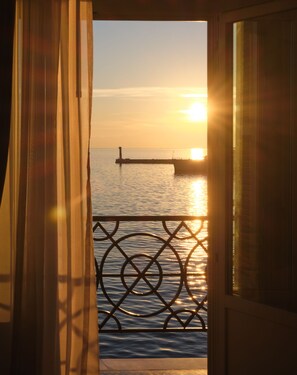 A view through a window with a metal railing, a body of water, and a distant structure.