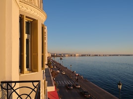 A coastal cityscape with a prominent building featuring a balcony with a wrought iron railing.