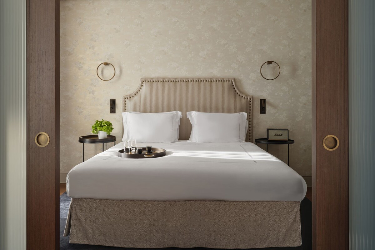 A neatly made bed with a headboard, two bedside tables with lamps, and a small plant on one table.