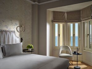 A bedroom with a bed, a chair, a small table, a potted plant, and a view of the sea through large windows. - ON Residence (Thessaloniki)