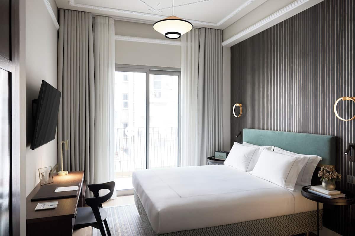 Une chambre d’hôtel avec un grand lit, un bureau avec une chaise, un téléviseur fixé au mur et une vue sur la ville par la fenêtre.