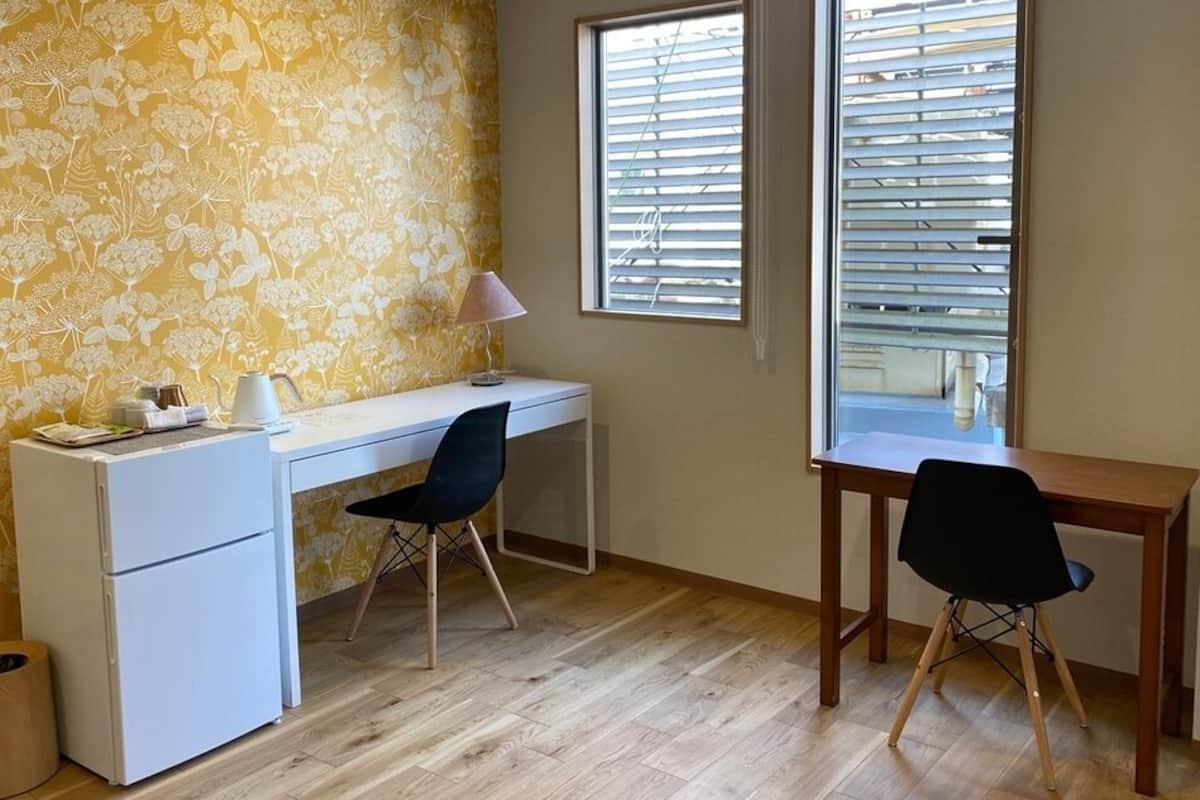 A room with a desk, two chairs, a small refrigerator, and a window with blinds.