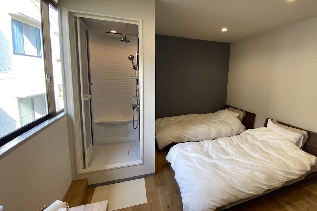 A bedroom with two beds, a shower, and a window.