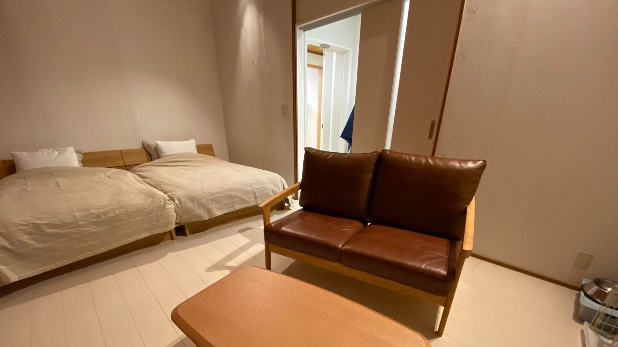 A bedroom with a bed, a brown leather sofa, and a wooden table.