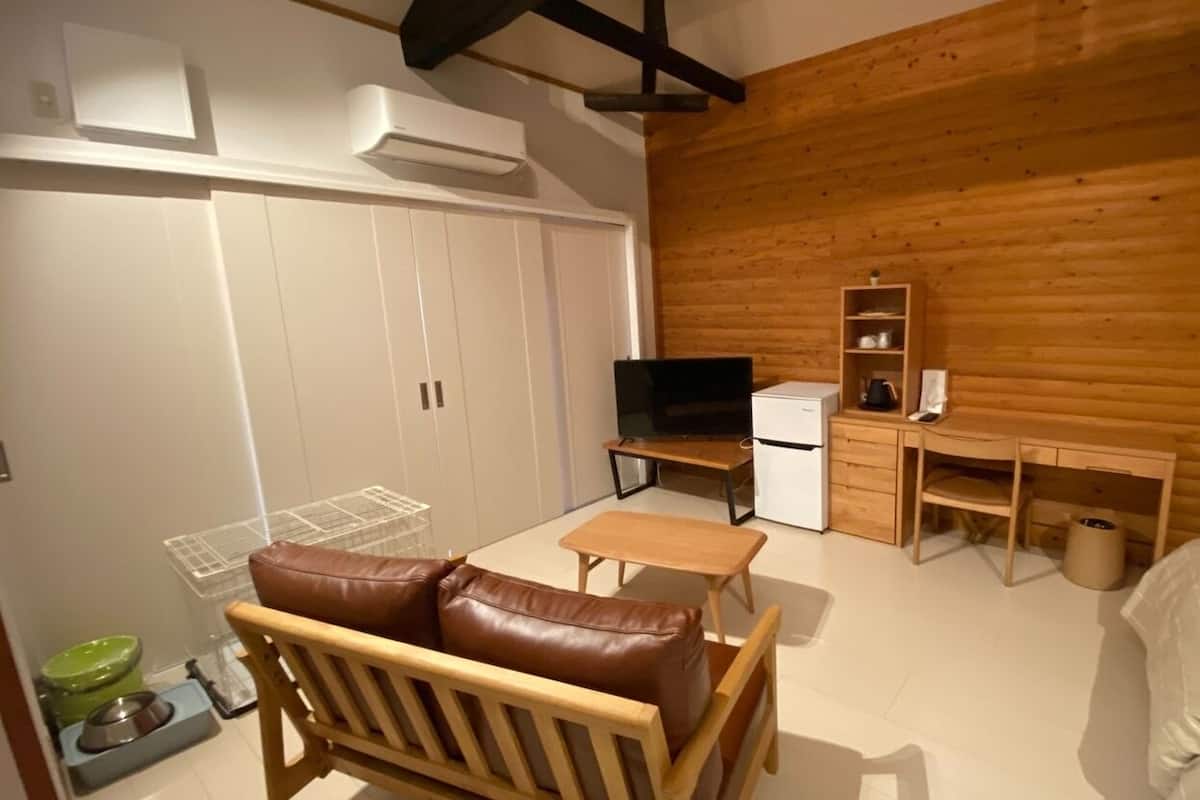 A compact room with a bed, a wooden desk, a television, and a pet feeding station.