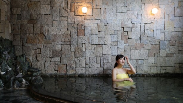A person in a stone-walled indoor pool with two wall-mounted lights.