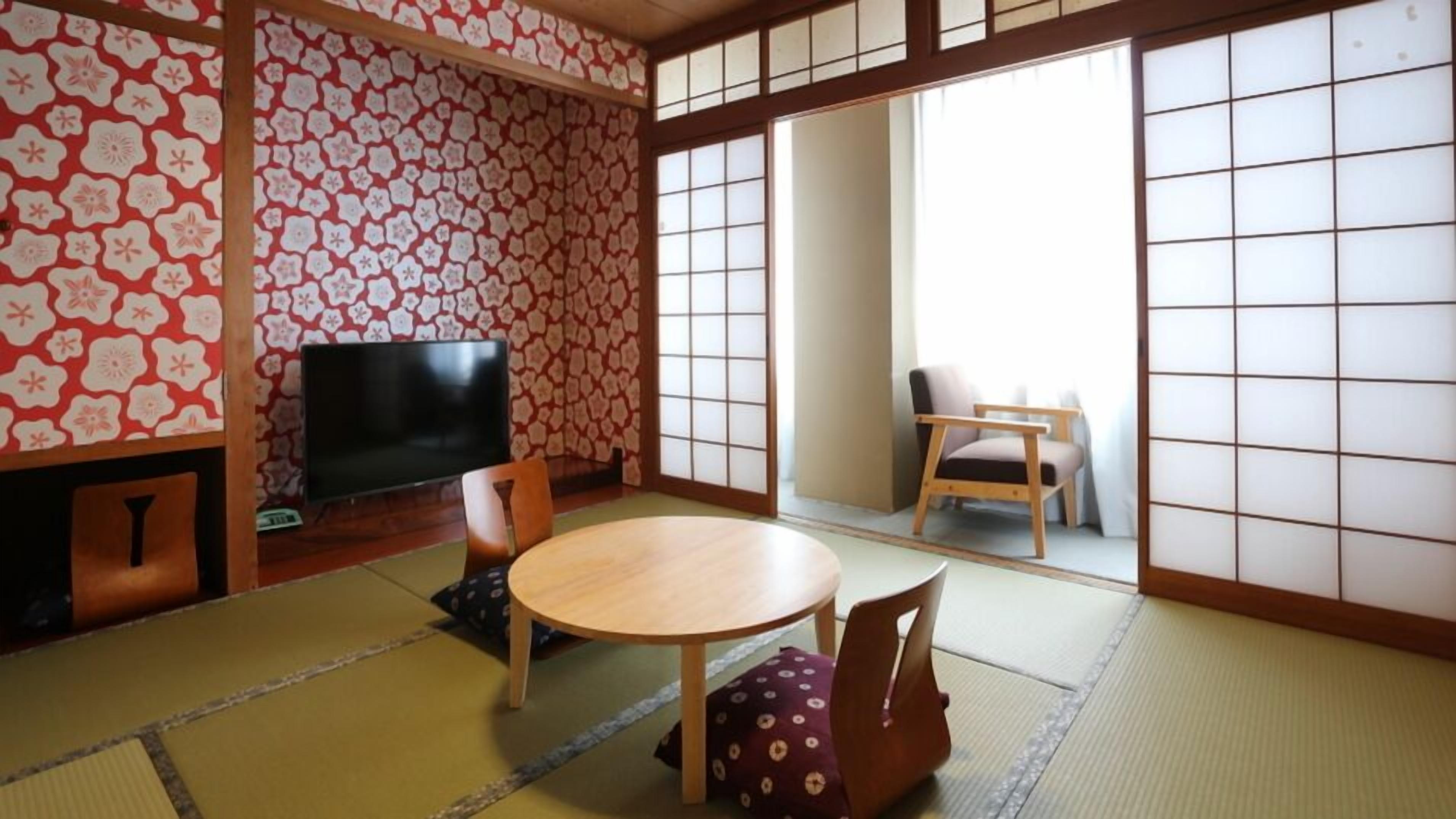 A traditional Japanese room with tatami flooring, a low table, a television, and sliding doors.